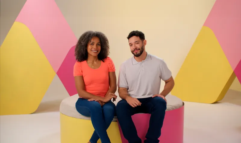 Casal sentado em banquetas coloridas durante gravação em estúdio