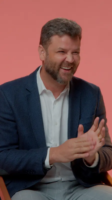 Homem de blazer conversando diante de um fundo vermelho