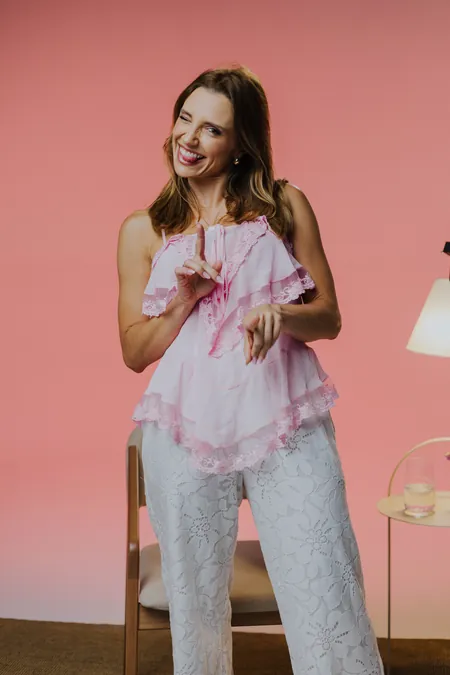 Mulher sorrindo em estúdio, de blusa rosa diante de um fundo na mesma cor